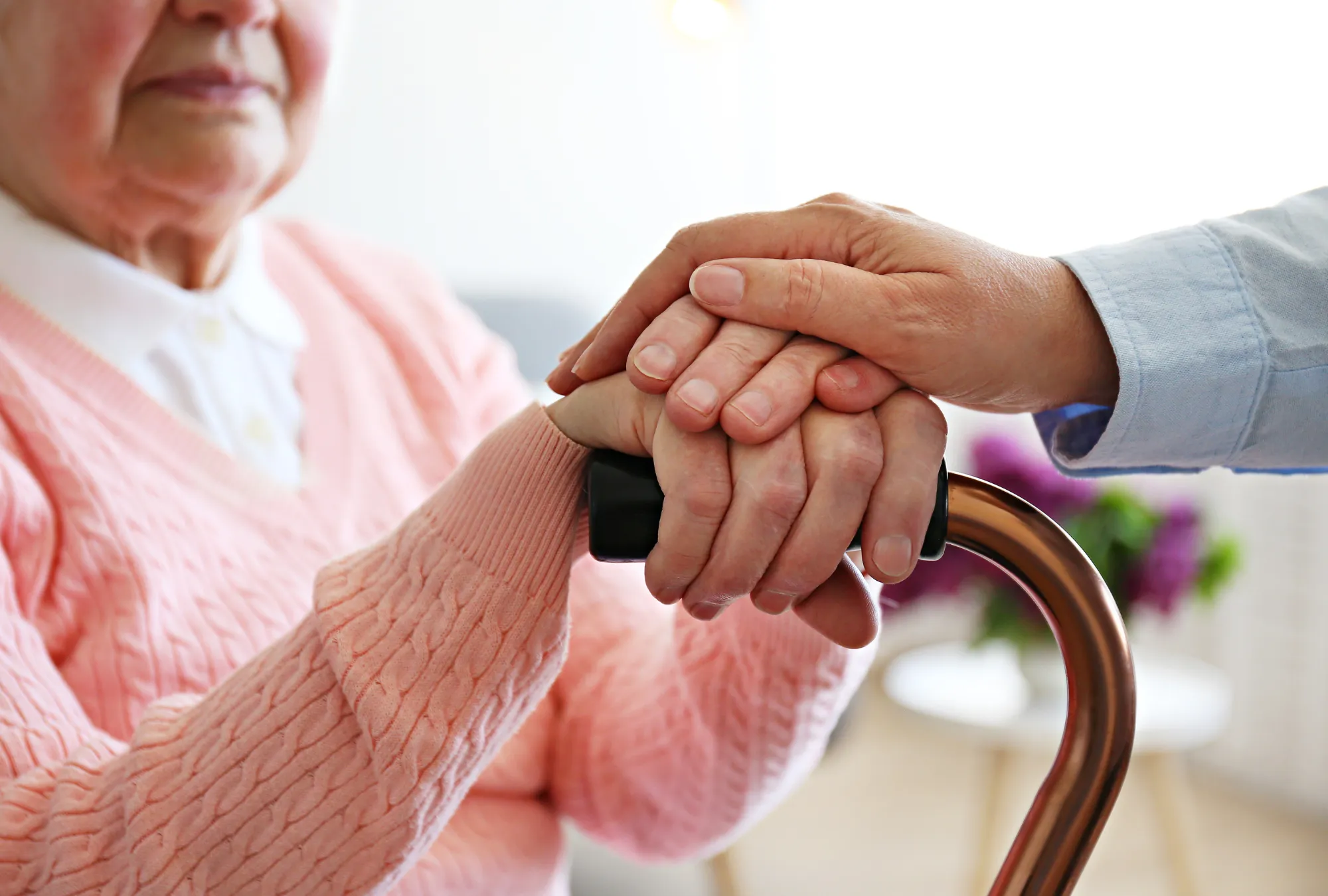 elderly woman holding a cane and hands with an aide